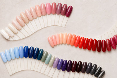 Curved rows of colorful nail swatches on a light neutral background, featuring soft, bold, and dark gel polish shades.