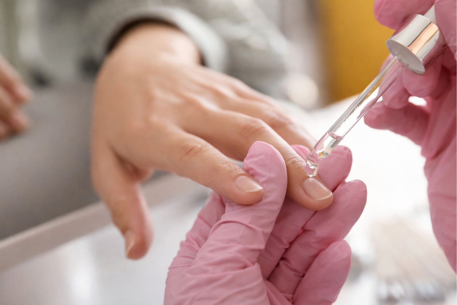 Nail technician applying cuticle oil to a client’s fingernails with a dropper in a clean salon setting