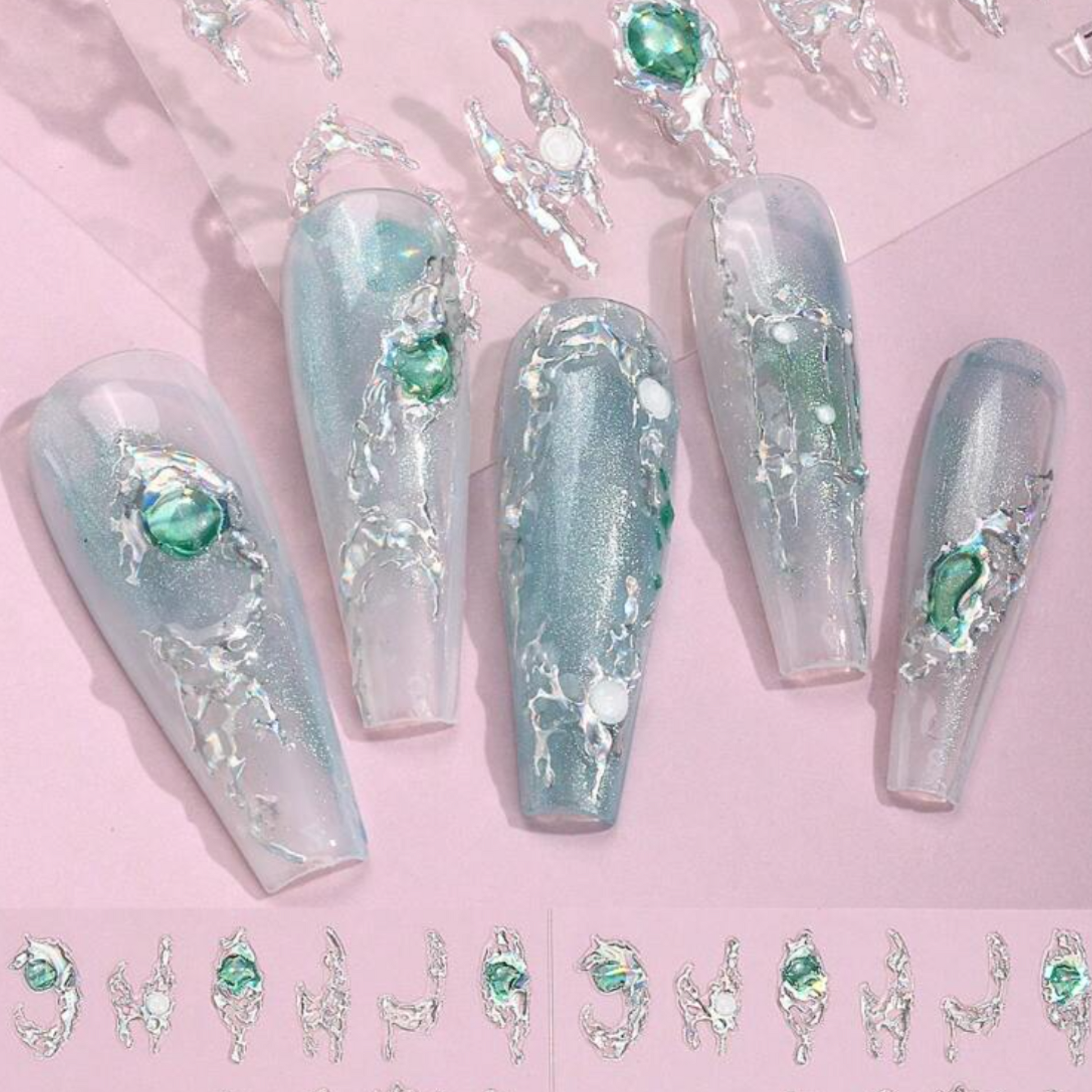 Decorative nails with green gemstones and silver accents on a pink background